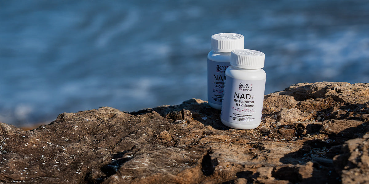 Frascos blancos de suplemento NAD+ Resveratrol & Colágeno sobre un tronco de madera rugoso en la orilla del mar, con el océano azul de fondo.