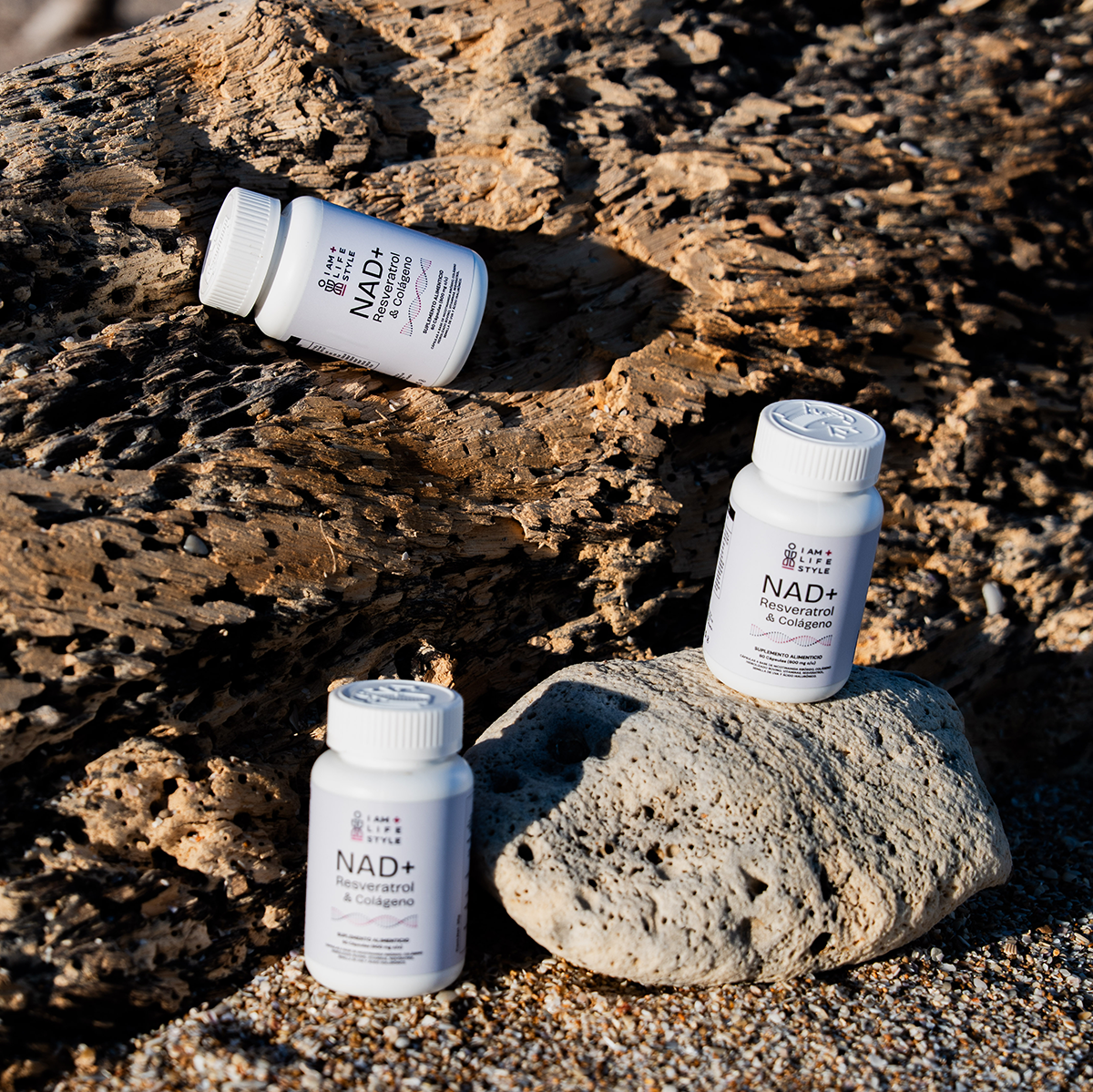 Frascos blancos de suplemento  NAD+ Resveratrol & Colágeno sobre un tronco de madera en la playa.